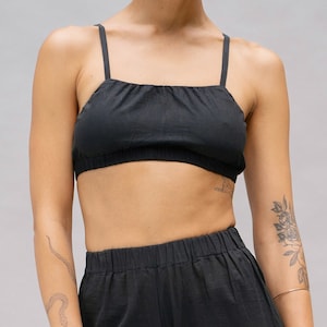 May include: Black two-piece outfit featuring a crop top with thin straps and high-waisted, wide-leg pants. The fabric appears to be a lightweight material. The outfit is a solid black color.