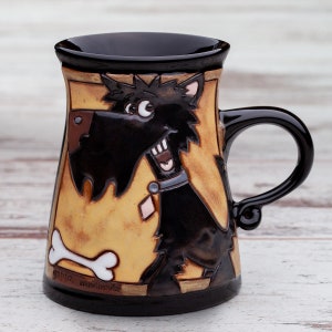 Puede incluir: Una taza de cer&aacute;mica negra y marr&oacute;n con un perro negro de dibujos animados con un hueso en la parte delantera. La taza tiene el texto "Ceramics, handmade" en la parte inferior.