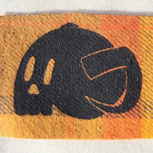 May include: A black and orange plaid fabric with a black silhouette of a pumpkin with a face.