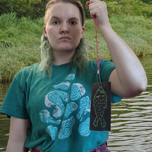 The artist holding a fish patch attached to a string like a stereotypical photo of a man holding a fish they caught.
