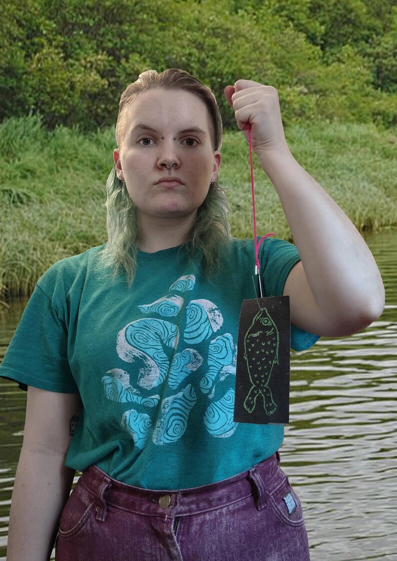 The artist holding a fish patch attached to a string like a stereotypical photo of a man holding a fish they caught.