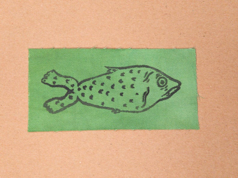 Fabric patch of an uncomfortable looking fish with feet in the colour Green.