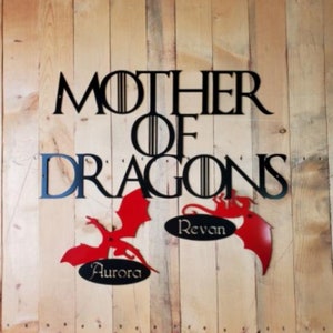 May include: Black metal wall art with the words "Mother of Dragons" and two red dragon silhouettes with the names "Aurora" and "Revan" underneath.