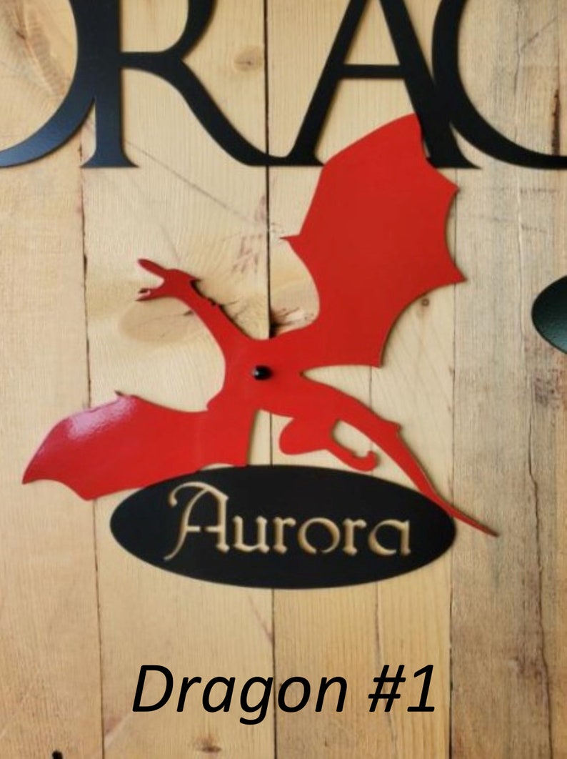 May include: Red metal dragon silhouette with black metal wings and a black oval with the word "Aurora" in gold lettering. The dragon is mounted on a wooden surface. The text "Dragon #1" is below the dragon.