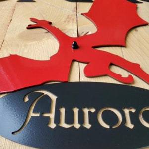May include: Red metal dragon silhouette with black metal wings and a black oval sign with the name "Aurora" cut out.