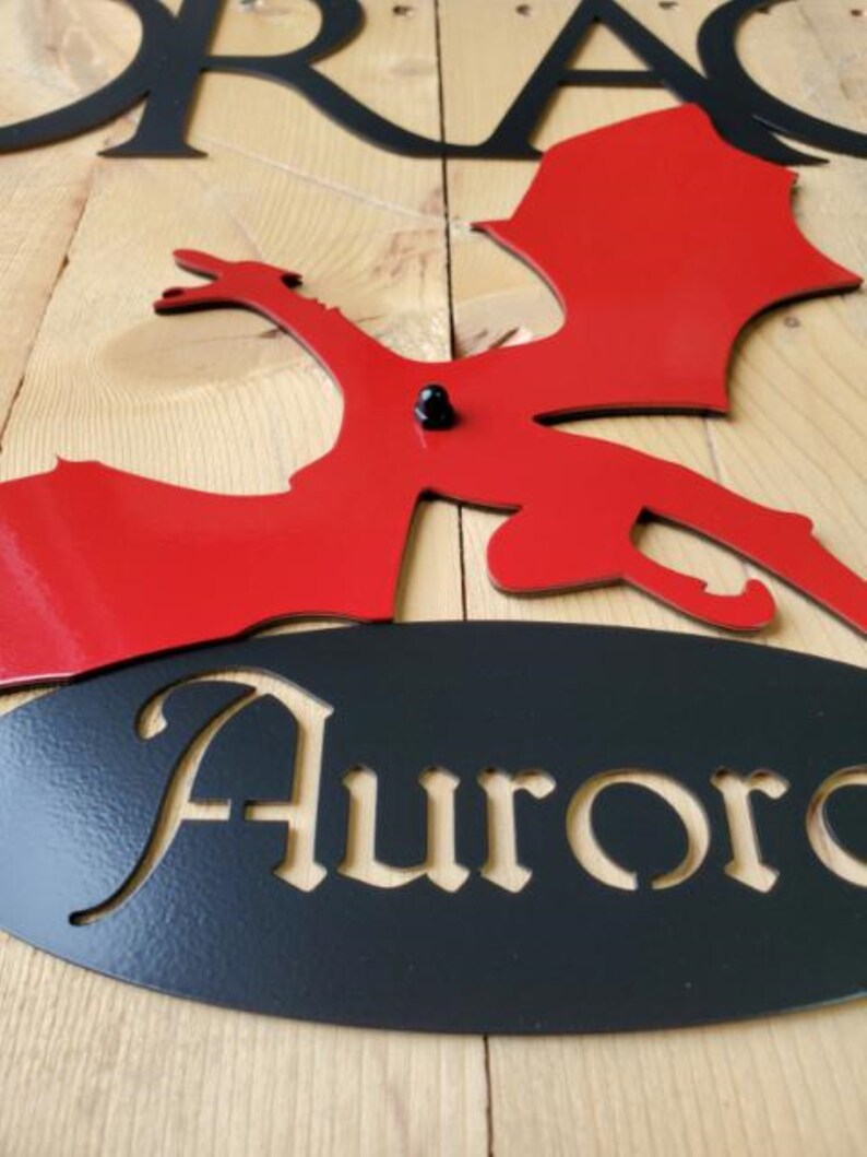 May include: Red metal dragon silhouette with black metal wings and a black oval sign with the name "Aurora" cut out.