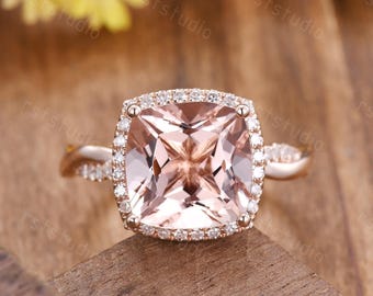 May include: A rose gold engagement ring with a square-shaped morganite center stone surrounded by a halo of smaller diamonds. The band is twisted and features additional diamonds.