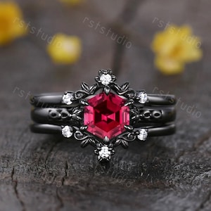 May include: Black ring set with a large red hexagonal gemstone surrounded by smaller white gemstones. The ring features a floral design.