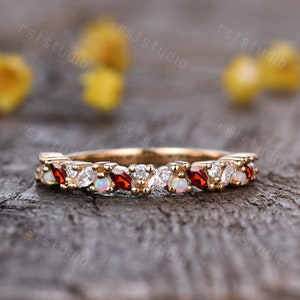 May include: A delicate gold band ring with a row of alternating red gemstones and white opals. The ring is set on a wooden surface.