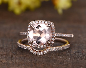 May include: A rose gold engagement ring set with a large, square-cut, pale pink morganite gemstone surrounded by a halo of smaller diamonds. The ring is paired with a matching rose gold band with a row of diamonds.