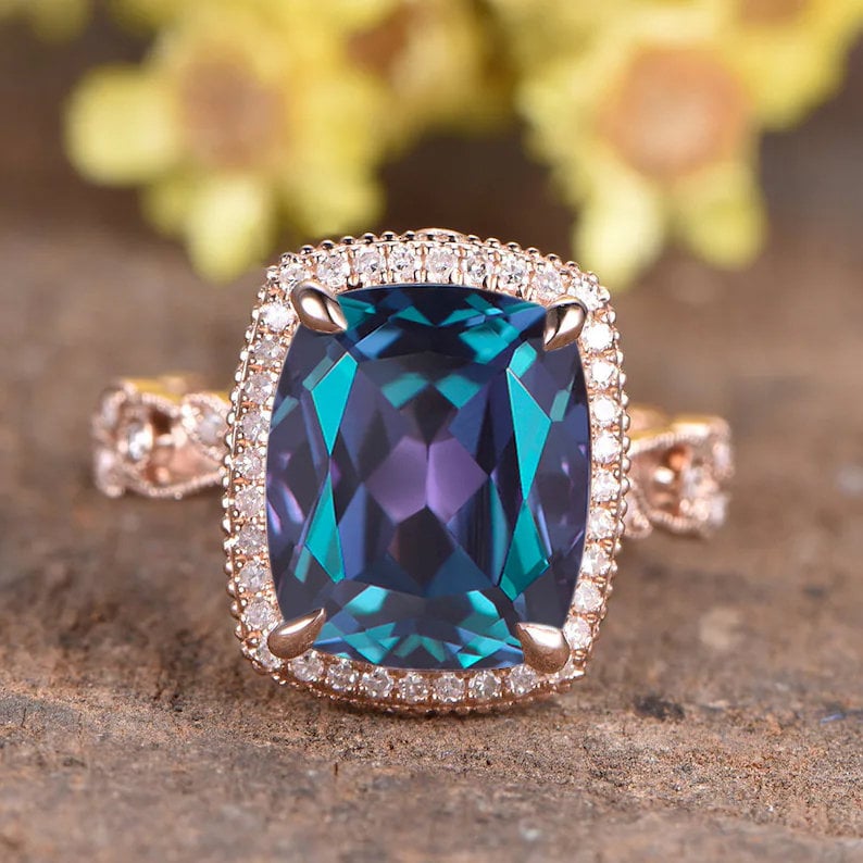 May include: A rose gold engagement ring featuring a large, cushion-cut alexandrite gemstone surrounded by a halo of smaller diamonds.