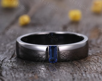 May include: A black band ring with a single blue sapphire gemstone set in the center.