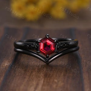 May include: Black ring set with a red gemstone. The ring features a hexagonal shaped gemstone with a black band and a delicate black band with a v-shaped design.