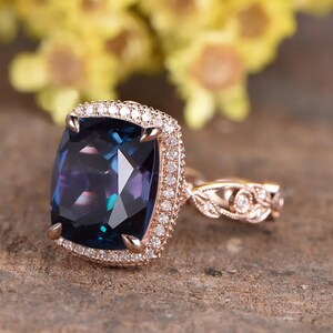 May include: A rose gold engagement ring featuring a large, cushion-cut, dark blue gemstone surrounded by a halo of smaller diamonds. The band has a delicate, floral design with additional diamonds.