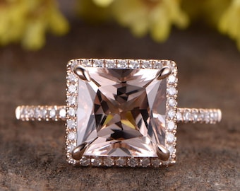 Könnte beinhalten: Ein Verlobungsring aus Roségold mit einem quadratischen Morganit-Mittelstück, das von einem Heiligenschein aus kleineren Diamanten umgeben ist. Die Ringschiene ist ebenfalls mit kleineren Diamanten besetzt.