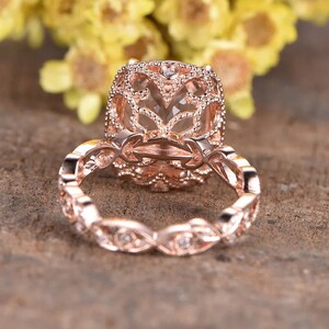 May include: Rose gold engagement ring featuring a large, clear, oval-shaped gemstone set in a delicate, filigree design. The band is adorned with smaller diamonds.