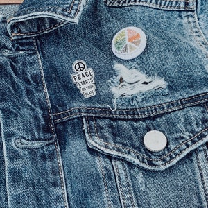 May include: A blue denim jacket with two pins. One pin says "Peace Starts On Your Plate" and the other is a colourful peace sign with the text "Peace Starts With You".