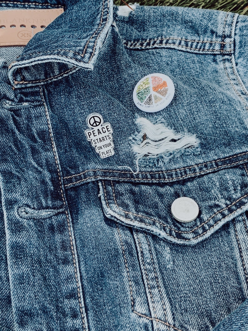 May include: A blue denim jacket with two pins. One pin says "Peace Starts On Your Plate" and the other is a colourful peace sign with the text "Peace Starts With You".
