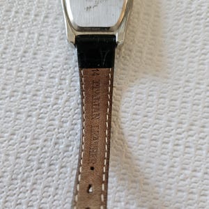 May include: A silver watch with a black leather strap. The watch face is rectangular with a silver bezel. The back of the watch has the number 25238 and the words "Stainless Steel Back" and "Quartz Japan". The strap is brown with the text "14 BYSHAN ZARA".