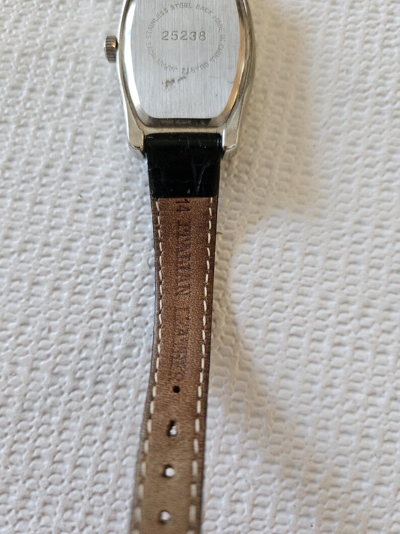 May include: A silver watch with a black leather strap. The watch face is rectangular with a silver bezel. The back of the watch has the number 25238 and the words "Stainless Steel Back" and "Quartz Japan". The strap is brown with the text "14 BYSHAN ZARA".