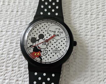 May include: Black Lorus Quartz watch featuring Mickey Mouse. The watch face has a white background with black polka dots and the text "IT'S TIME FOR FUN!". Mickey Mouse is depicted in his classic outfit. The watch band is black with white polka dots.