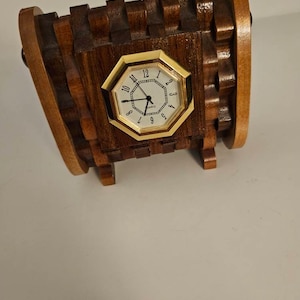 May include: A wooden clock with a gold-colored octagonal face and a white clock face. The clock is made of dark and light brown wood and has a unique, geometric design. The clock is a decorative item.