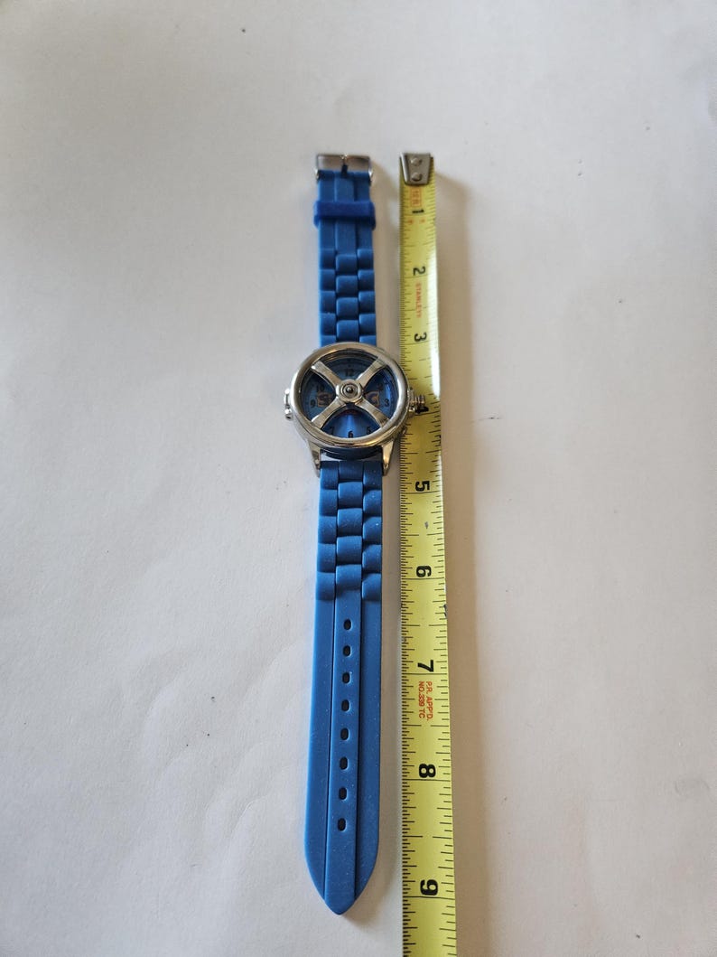 Puede incluir: Un reloj de pulsera azul con esfera plateada y correa de silicona azul. El reloj est&aacute; junto a una cinta m&eacute;trica amarilla, que muestra que la correa mide aproximadamente 23 cm.