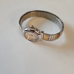May include: A silver and gold two-tone watch with a white face and a metal band.