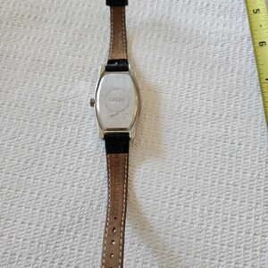 May include: A rectangular silver watch with a black leather strap. The watch face is not visible. The back of the watch has the number "25238" printed on it. The watch strap is brown on the inside.