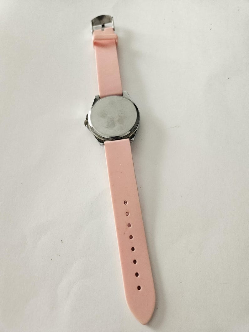 Op de afbeelding: Een polshorloge met een lichtroze siliconen band en een zilverkleurige metalen kast. De horlogeband wordt vastgezet met een zilveren gesp. De wijzerplaat van het horloge is niet zichtbaar op deze afbeelding.