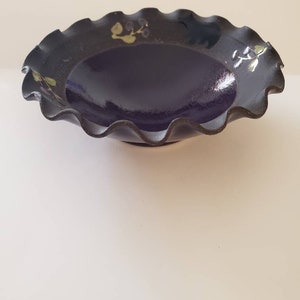 May include: A black ceramic bowl with a ruffled edge and a dark purple glaze. The bowl has a floral design painted in gold and green.