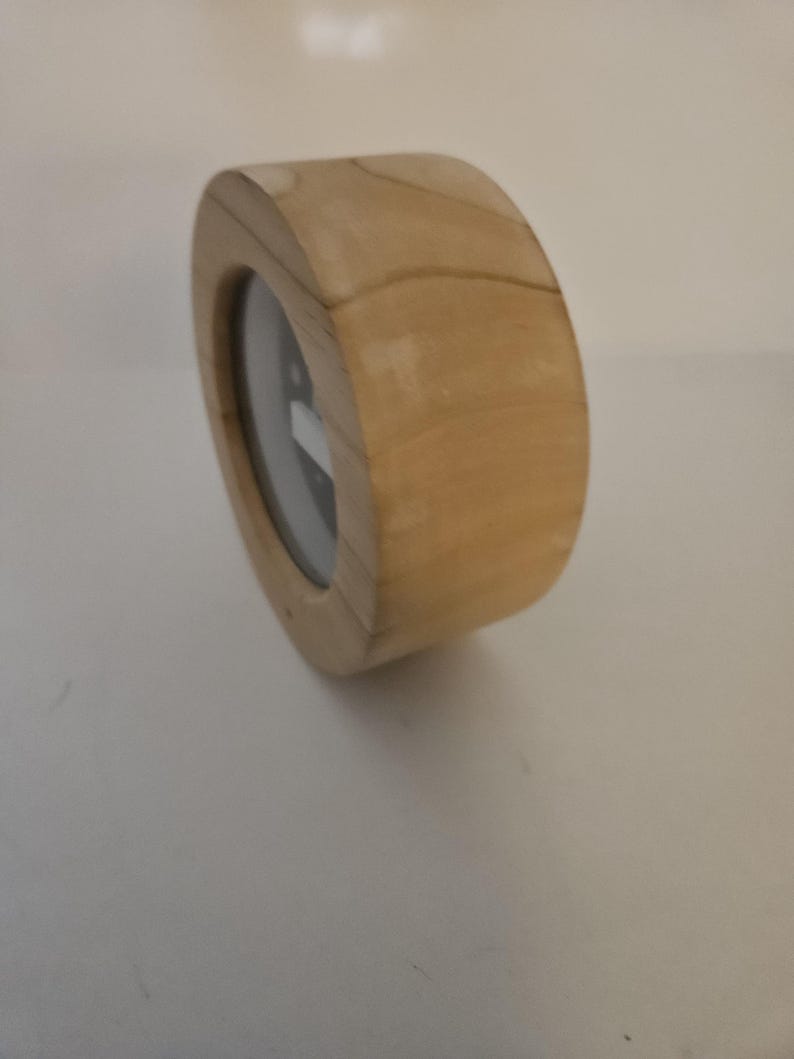 Puede incluir: Un reloj de madera con un acabado marr&oacute;n claro. El reloj tiene una forma rectangular redondeada con una esfera circular. La esfera es negra con marcas y manecillas blancas. El reloj est&aacute; hecho de madera.