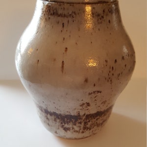 May include: A white ceramic jar with a lid, featuring brown speckles and a darker brown band around the bottom.