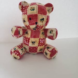 May include: A ceramic teddy bear piggy bank with a patchwork design featuring red and white squares with small bear and house illustrations.