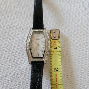 May include: A rectangular quartz watch with a silver bezel set with rhinestones. The watch face is white with black numerals and hands. The black leather strap is approximately 20 cm long.