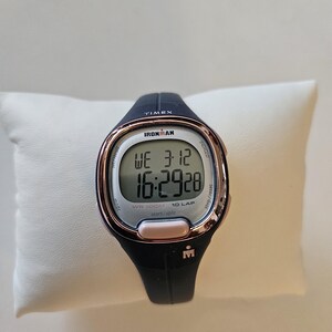 May include: A black and rose gold Timex Ironman watch with a digital display showing the time, date, and lap counter. The watch is water resistant to 300 meters.