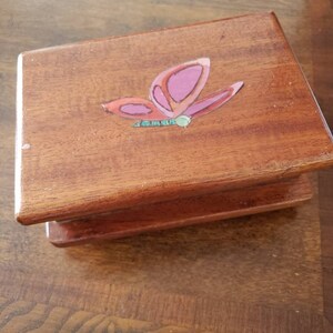 May include: A wooden box with a butterfly design painted on the top. The butterfly is pink, red, and green.