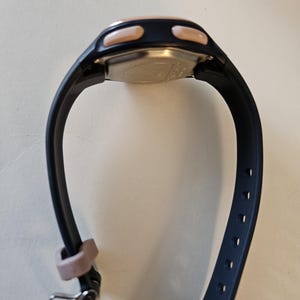 May include: A black and rose gold digital watch with a black silicone band. The watch has two buttons on the side and a silver buckle.