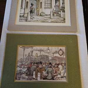 May include: Two framed vintage prints. The top print depicts a man outside a building. The bottom print shows a train station scene with people and a clock. Both prints have gold trim and are set in neutral-toned mats.