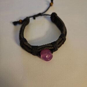May include: A black braided bracelet with a purple gemstone bead.