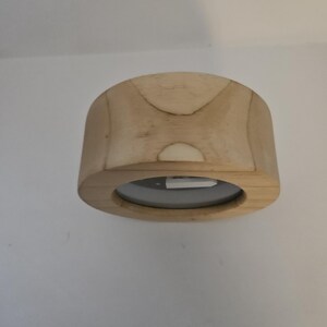 Puede incluir: Un tap&oacute;n de botella de madera clara con una abertura circular. El tap&oacute;n tiene una forma rectangular redondeada con una base plana y una parte superior curvada. La veta de la madera es visible y el tap&oacute;n parece inacabado.