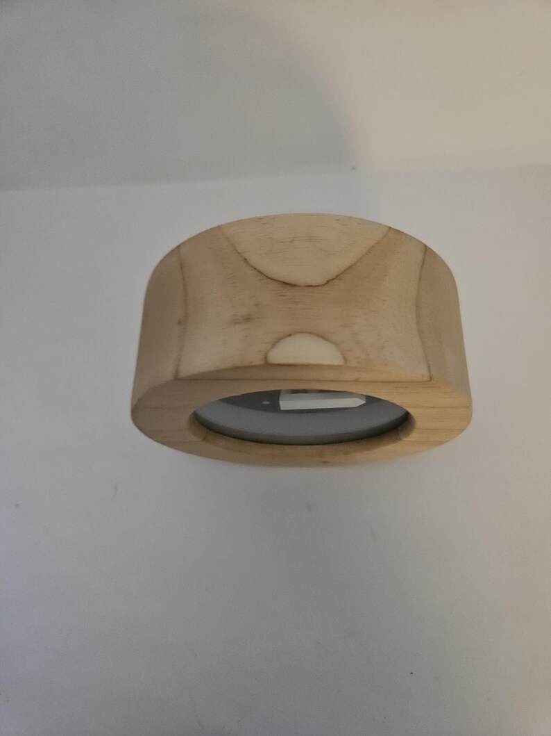 Puede incluir: Un tap&oacute;n de botella de madera clara con una abertura circular. El tap&oacute;n tiene una forma rectangular redondeada con una base plana y una parte superior curvada. La veta de la madera es visible y el tap&oacute;n parece inacabado.