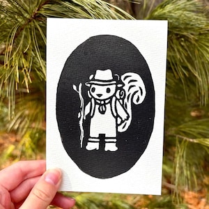 May include: A black and white print of a cartoon squirrel dressed as a hiker, holding a walking stick and wearing a hat and backpack. The image is set within a black oval on a white background.