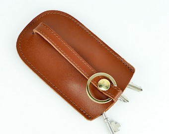 May include: A brown leather key holder with a metal ring and two keys. The key holder has a strap that can be used to attach it to a belt loop.