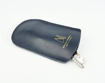 May include: A dark blue leather key holder with the text "Village Leather Made in London" in gold lettering.