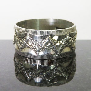 May include: A silver ring with a geometric pattern. The ring is wide and has a smooth, polished finish.