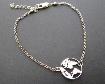 May include: A silver chain bracelet with a circular pendant featuring a cut-out design of the world map.