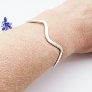 Op de afbeelding: Een zilveren armband met een golvend ontwerp. De armband is open en verstelbaar.