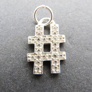 May include: Silver charm in the shape of a hashtag with clear crystals around the edges. The charm has a loop at the top for attaching to a bracelet or necklace.