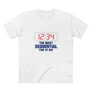May include: A white short-sleeve t-shirt featuring a graphic of a digital clock display showing 12:34 in red, enclosed in a thin black rectangle. Below the clock, the text reads THE MOST SEQUENTIAL TIME OF DAY in bold blue capital letters.